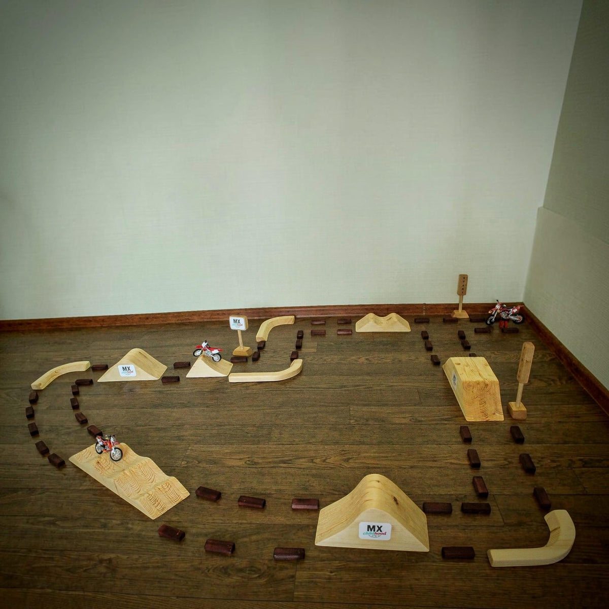 Large handmade wooden motocross track for kids with multiple dirt bike jumps, ramps and obstacles. A child playing with miniature motocross bikes on a large indoor racing track, a unique Christmas gift for kids 2026.