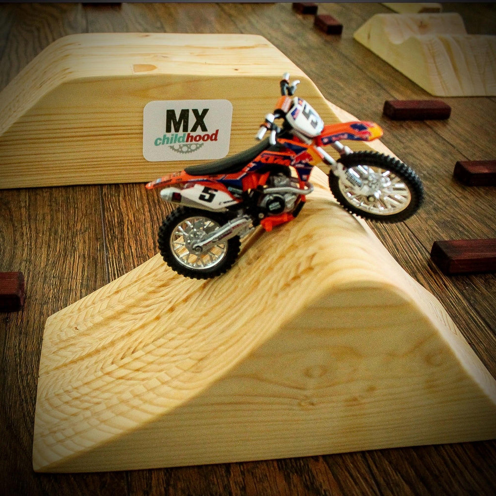 Dirt bike model riding on a handmade wooden motocross track with jumps and racing obstacles.