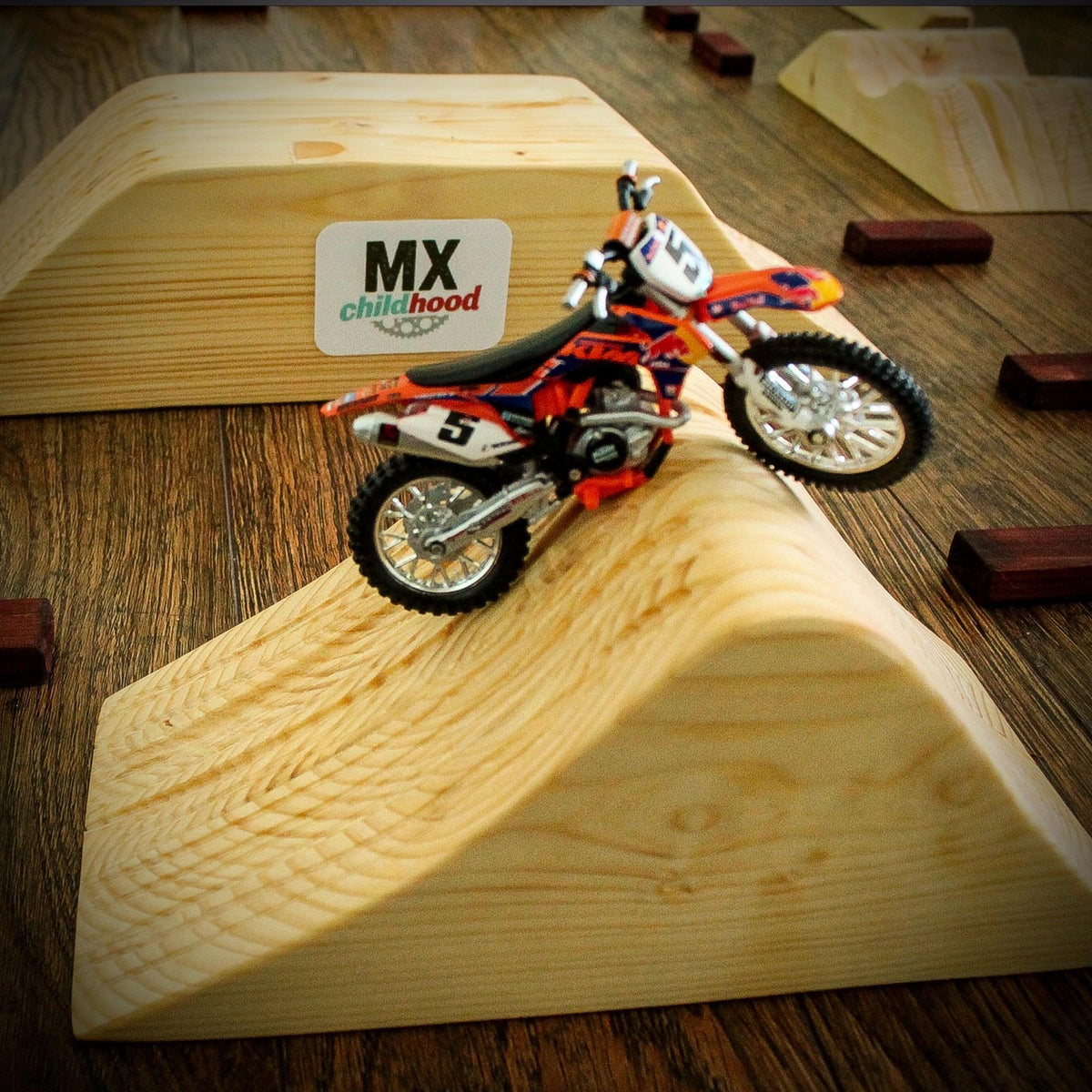 Dirt bike model riding on a handmade wooden motocross track with jumps and racing obstacles.